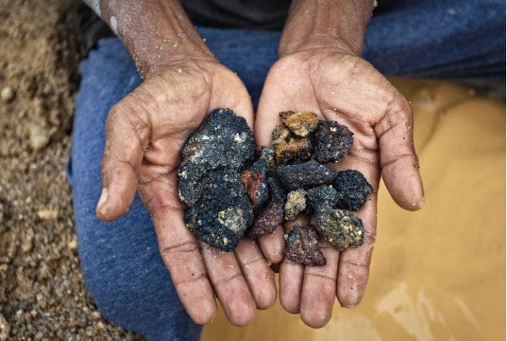 Miner shows rocks he found that contain tin. Source: friendsoftheearth.uk